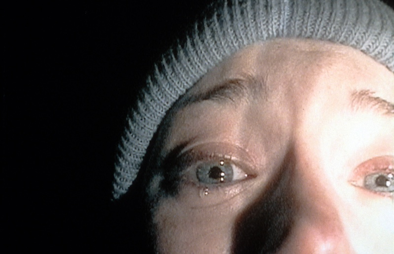 A close-up of a scared woman’s flashlight-illuminated face.