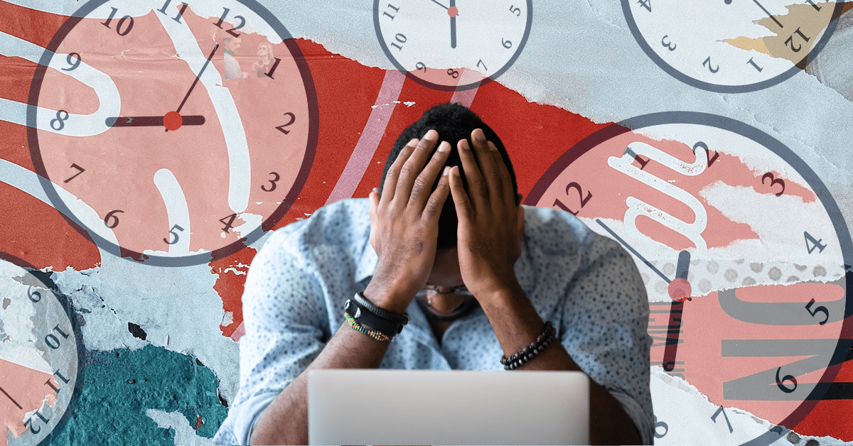 A Black man with his head in his hands in front of a laptop with clocks showing 8 o’clock in the background.