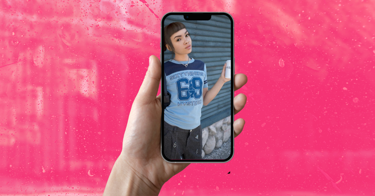 A hand holds a phone, its screen displaying a photo of virtual influencer Miquela, against a pink background.