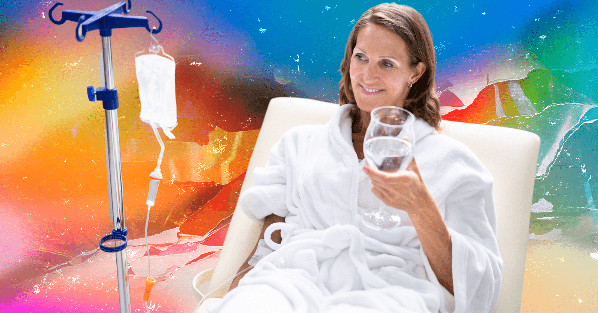 A white woman in a white robe drinking a glass of water with one hand with an IV in the other arm.