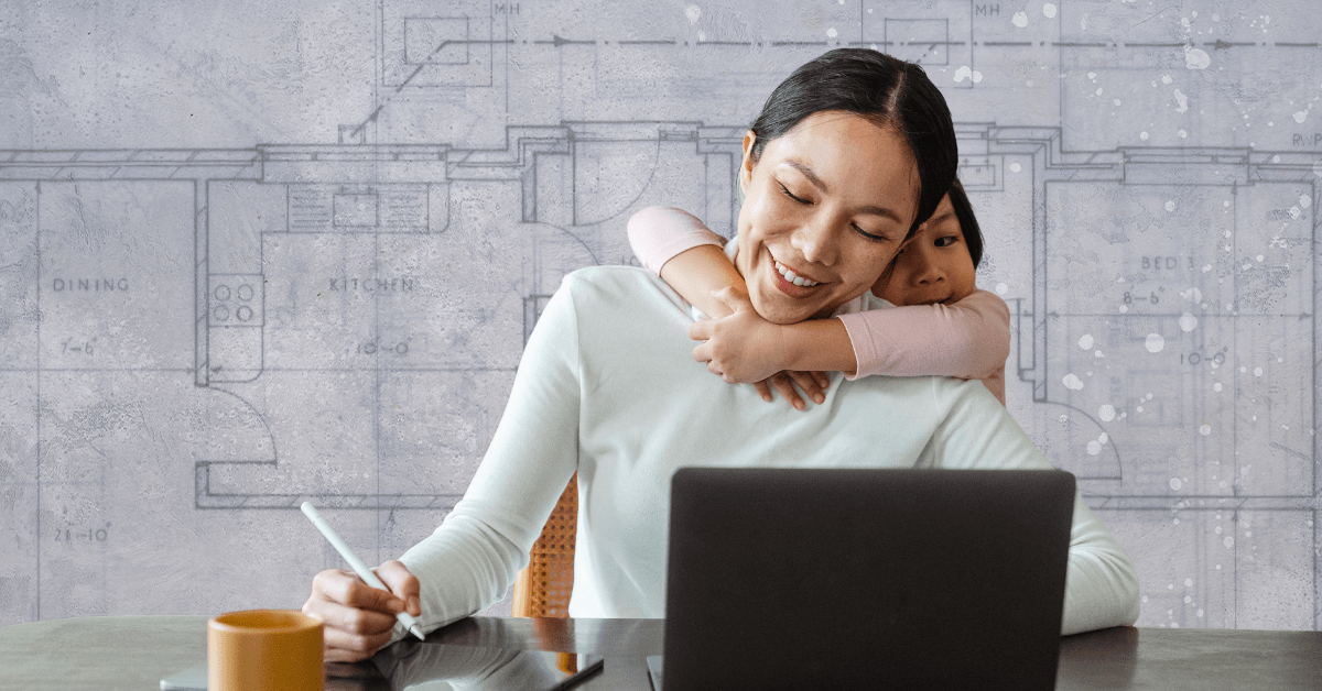 A woman smiling and writing on a notepad at her computer while a little girl hugs her from behind.