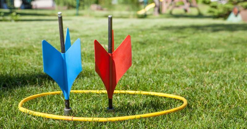 A blue and red lawn dart sticking out of a yellow ring in the grass.